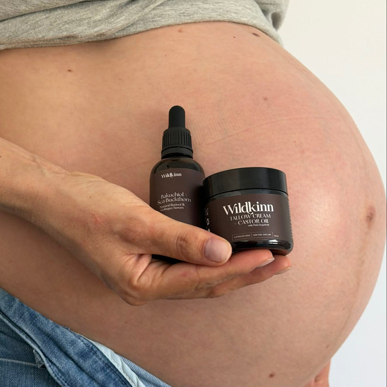 Pregnant person holding skincare products with 'Wilkinn' branding.