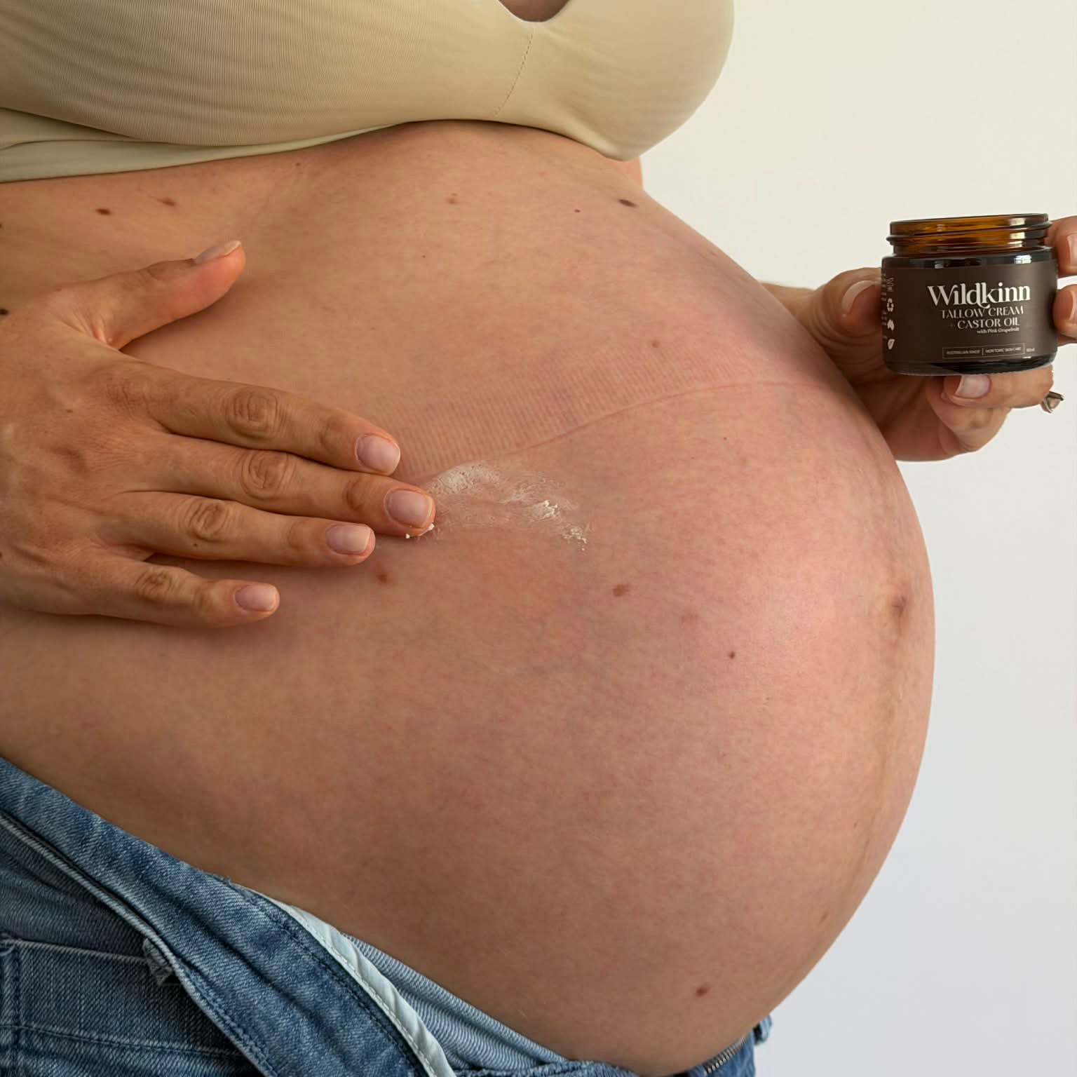 Pregnant person holding a jar of cream over their belly