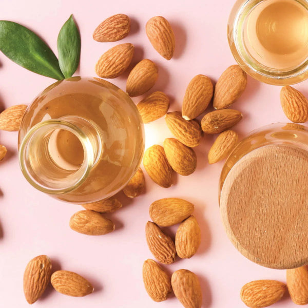 Glass jars of almond oil surrounded by whole almonds on a soft pink background – Wildkinn non-toxic skincare.