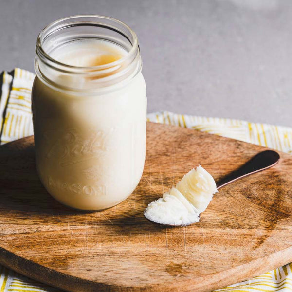 Glass jar of creamy rendered beef tallow with a spoonful on a wooden board – Wildkinn non-toxic skincare.