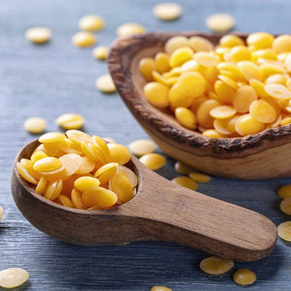 Natural yellow beeswax pellets in wooden spoon and bowl on a rustic surface – Wildkinn non-toxic skincare.