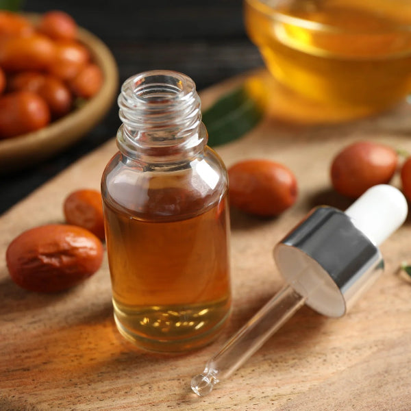 Glass bottle of golden jojoba oil with dropper, surrounded by jojoba seeds and leaves on a wooden surface – Wildkinn non-toxic skincare.