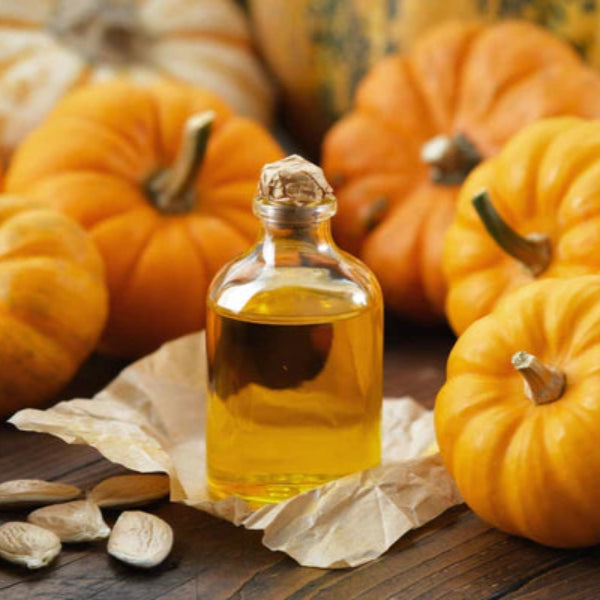 Glass bottle of pumpkin seed oil surrounded by fresh pumpkins and seeds on a rustic wooden table – Wildkinn non-toxic skincare.