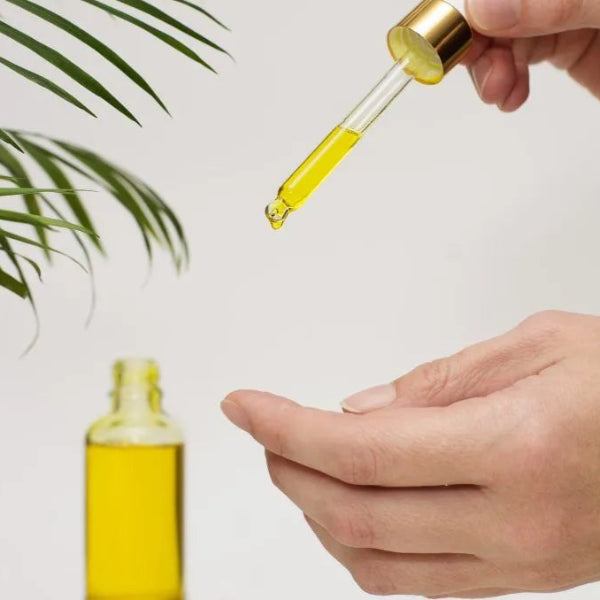 Hands applying golden yellow vitamin E oil from a glass dropper bottle – Wildkinn non-toxic skincare.