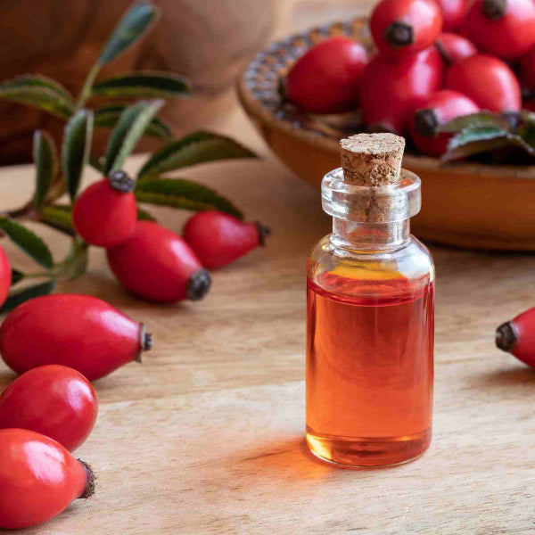 Glass bottle of rosehip oil surrounded by fresh rosehips on a wooden table – Wildkinn non-toxic skincare.